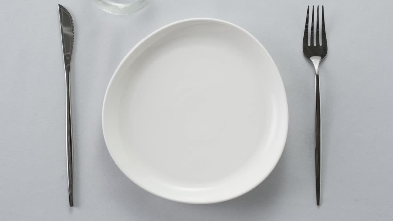 Elegant table setting with white tableware plates, cutlery, and glassware for a classy dining, fancy expensive restaurant dinner