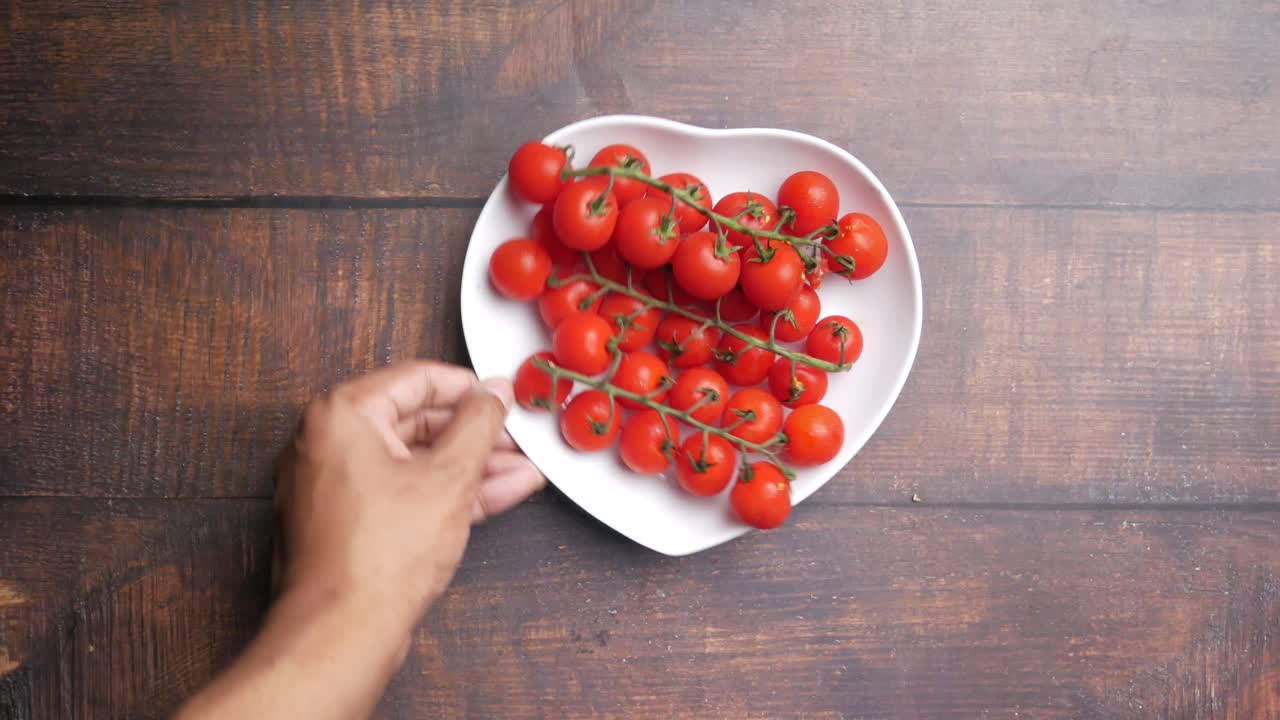 손은 심장 모양의 접시에 체리 토마토 한 어리에 도달