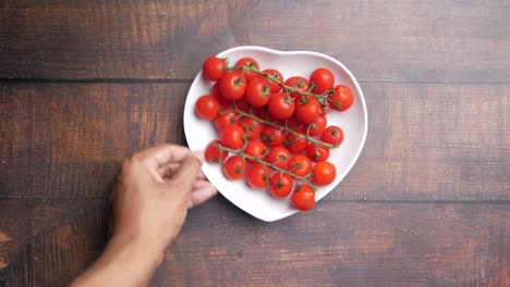 mano alcanzando un montón de tomates cereza en un plato en forma de corazón