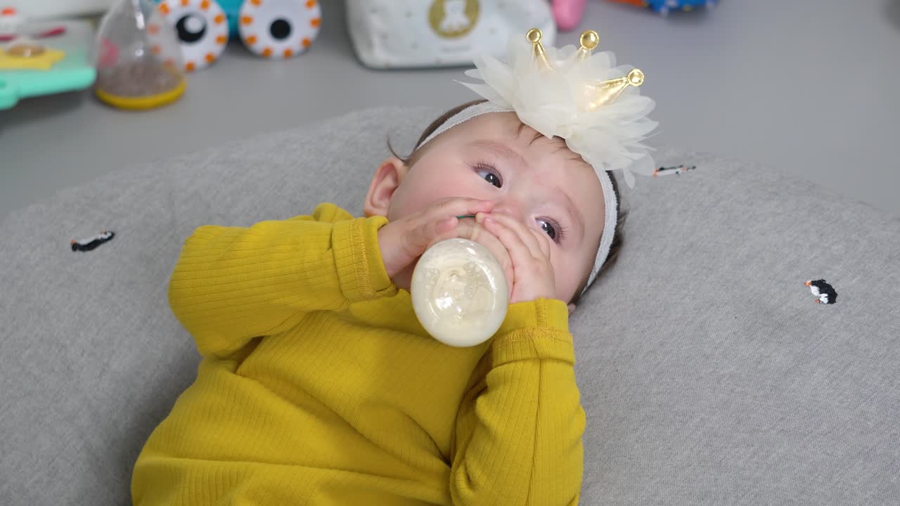 Bambino piccolo affamato che beve lentamente il latte dal biberon mentre è sdraiato su un comodo cuscino a ciambella grigio, in primo piano