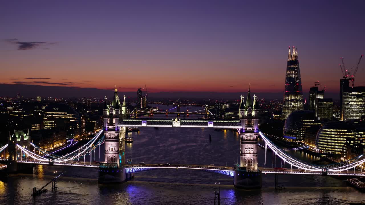 Aerial video view of illuminated Tower Bridge at dusk, capturing the vibrant cityscape and colorful