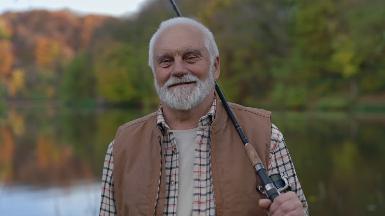 Smiling senior fisherman holding a fishing rod by a lake