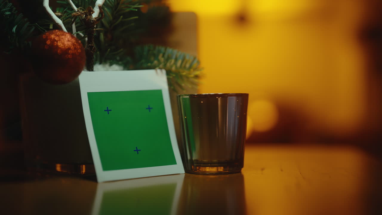 A green screen next to holiday decor with warm lighting and a glass cup indoors