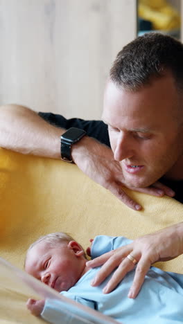 caring caucasian dad kneeled near the baby crib. happy parent talks to his newborn stroking his belly. vertical video