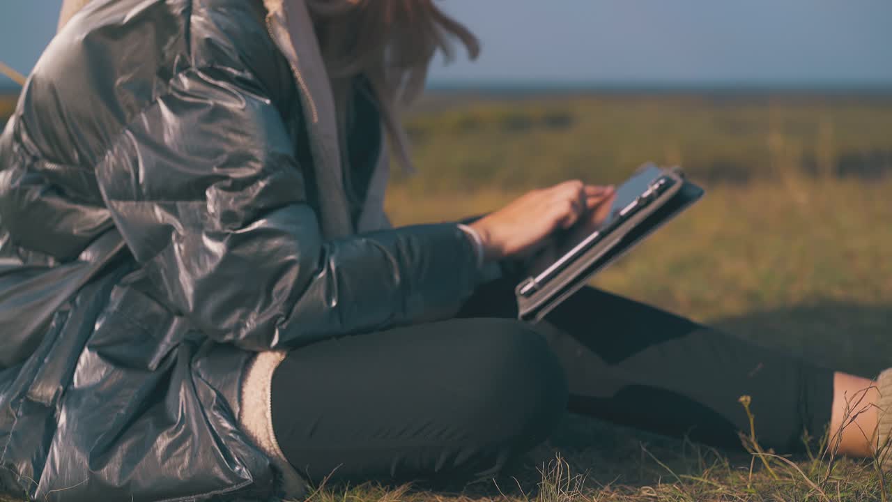 туристка работает на планшете, сидя на траве вблизи.