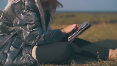 girl tourist works on tablet sitting on grass closeup