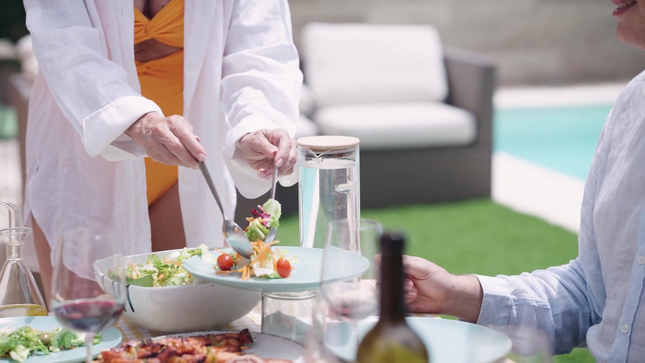 Woman Serving Fresh Salad to Friends at Outdoor Poolside Lunch