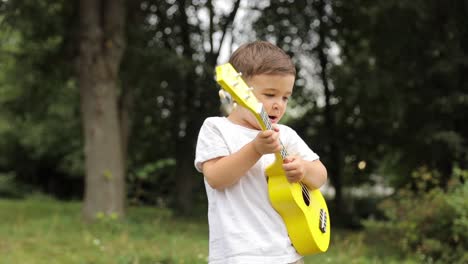 cute boy holding ukulele playing music in the park, carefree mind, concept of music playing, creative activity, children’s development.