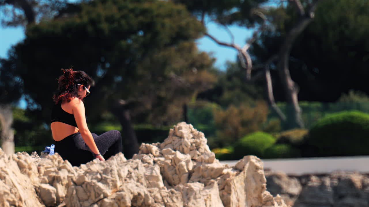 Woman wearing a black sportswear set resting on the rocks with trees on the background
