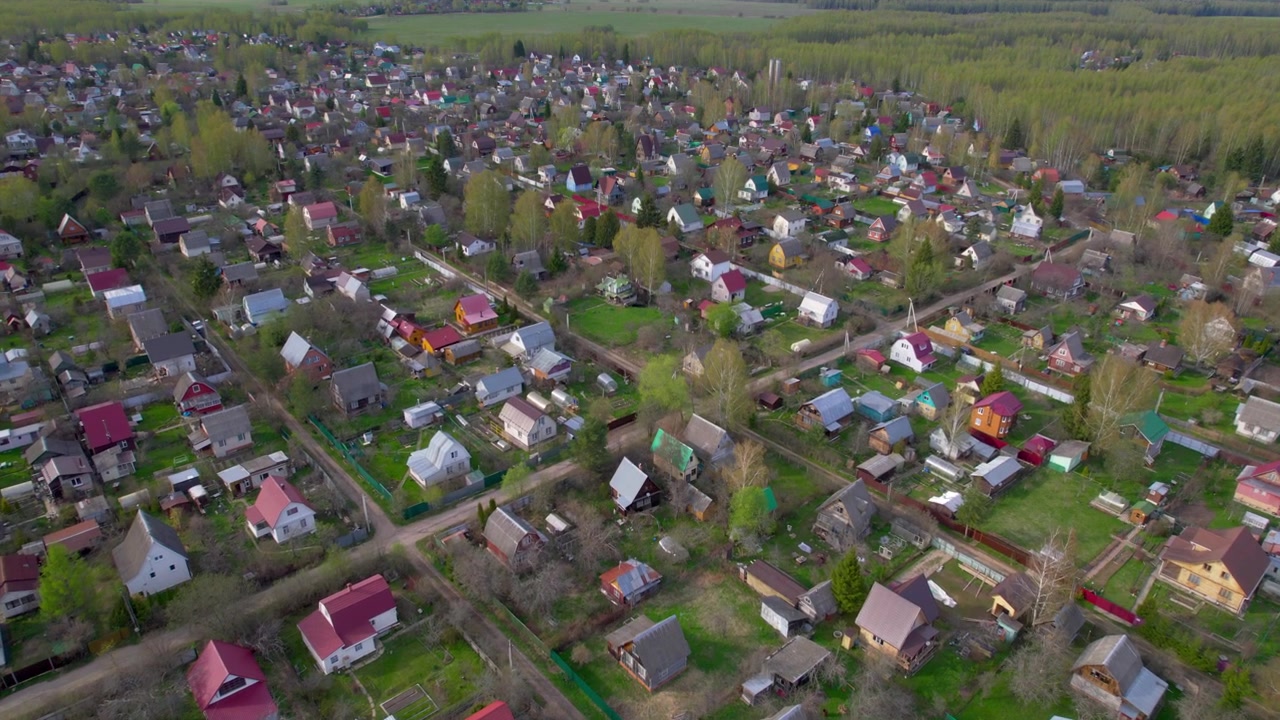 Lavt droneperspektiv passerer over landhuses haver og veje med skov bag landsbyen for landlig livsstil, boligejendomme og forårslandskabstemaer