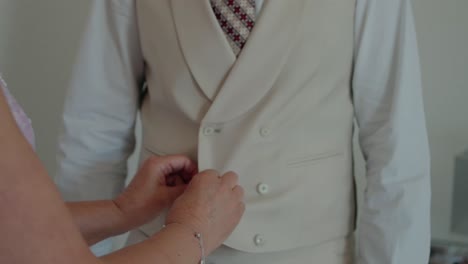 groom adjusting light beige suit jacket, preparing for wedding day