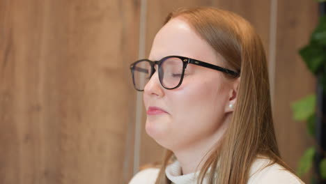 close up of woman in glasses gently smelling chocolate cake with eyes closed, savoring aroma with thoughtful expression while holding dessert plate, wooden wall background