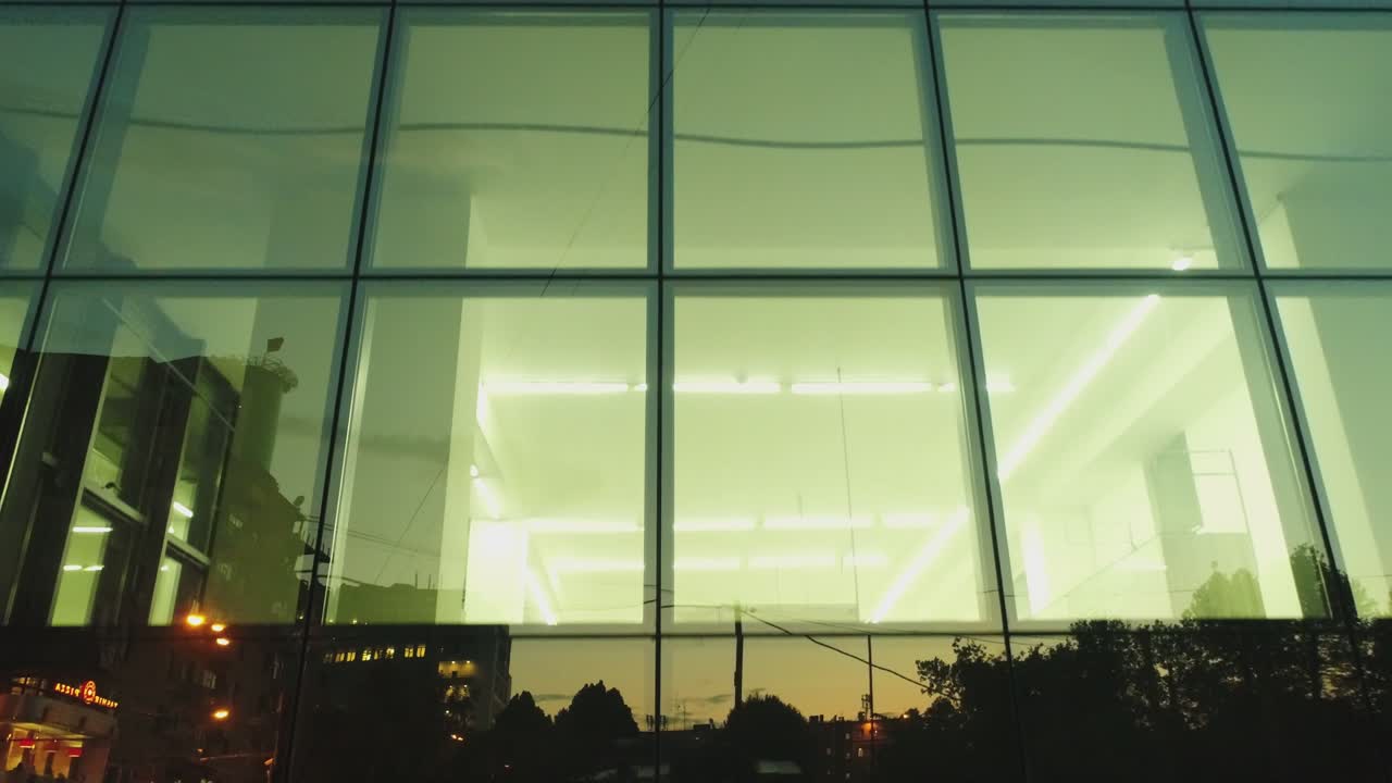 vista exterior de 4k del edificio del distrito comercial, centro comercial con ventanas de espejo de pared por la noche o por la noche. reflejo de la ciudad, la gente, los coches en las paredes espejadas. cámara de dron moviéndose. personas que trabajan dentro
