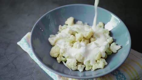 verter queso cremoso en coliflor cocido en un plato gris sobre un fondo oscuro