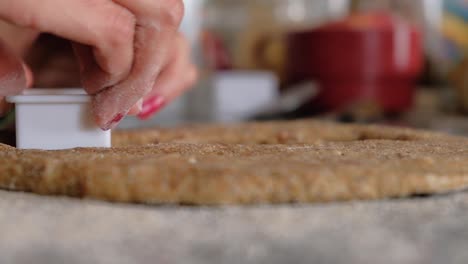 woman hands cutting cookies on whole wheat dough on floured countertop