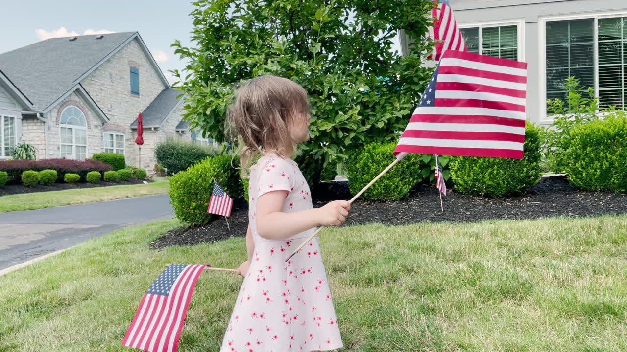A little girl waves American flags in her front yard before a parade or celebration