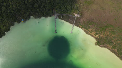 Aerial-birds-eye-overhead-top-down-descending-view-of-pastel-green-water-in-lake-and-people-relaxing-around-wooden-piers.-Kaan-Luum-lagoon,-Tulum,-Yucatan,-Mexico