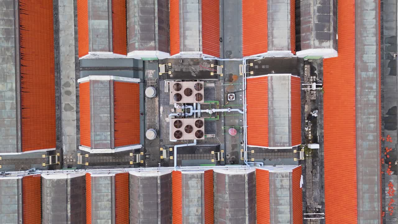 Drone top down rises above AC vent and fan units on top of orange tiled rooftop, industrial texture centered over building complex