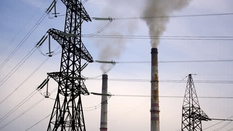 high-voltage towers and pipes of power station with smoke. chemical emissions from industry next to transmission lines on sky background.