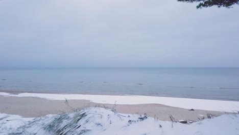 Hermosa-Vista-Aérea-De-La-Costa-Del-Mar-Báltico-En-Un-Día-De-Invierno-Nublado,-Playa-Con-Arena-Blanca-Cubierta-De-Nieve,-Erosión-Costera,-Cambios-Climáticos,-Tiro-De-Drones-De-Gran-Angular-Moviéndose-Hacia-Atrás