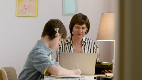 mature woman in striped shirt working with laptop and her daughter is doing her homework