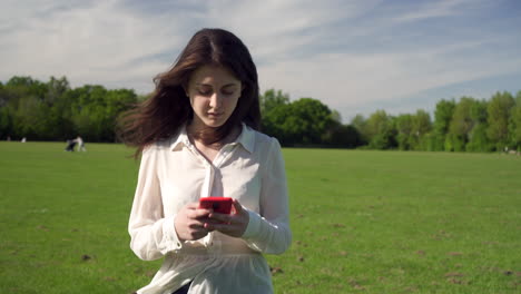 Happy-smiling-gorgeous-italian-girl-enjoying-walking-around-the-park-while-typing-text-via-smartphone-gadget,-positive-female-tourist-using-technology-to-communicate