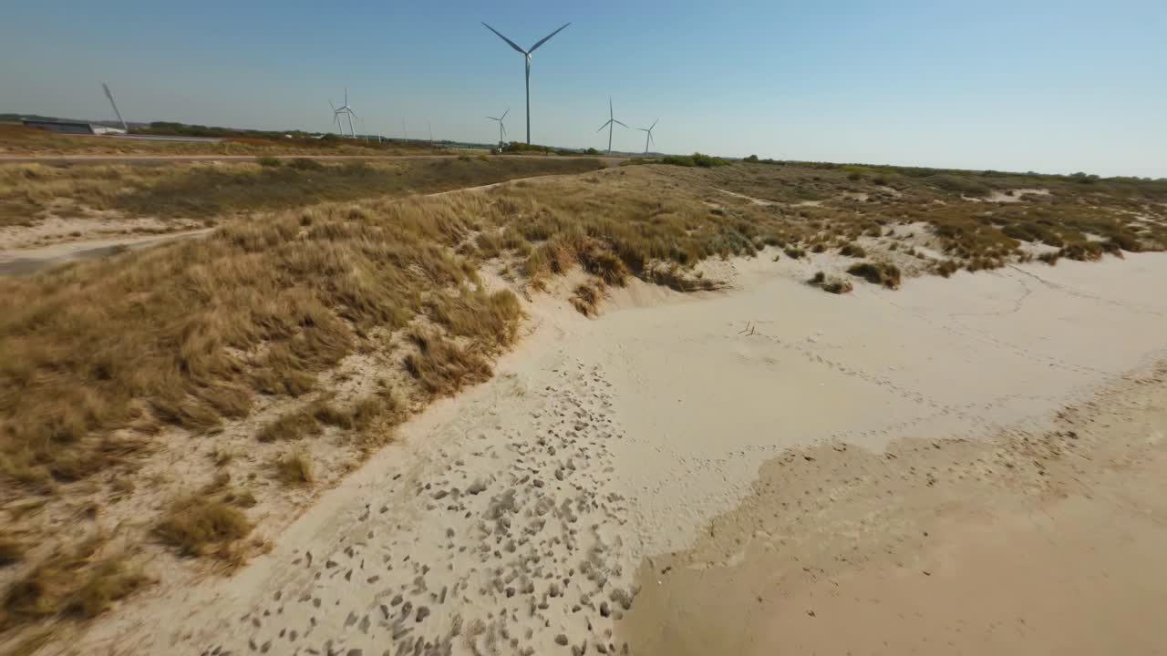 Aerial drone flight towards coastal wind park with spinning wind turbines