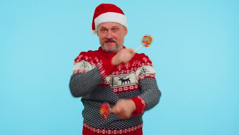 joyful man in red christmas sweater hat holding candy striped lollipops dancing making silly faces
