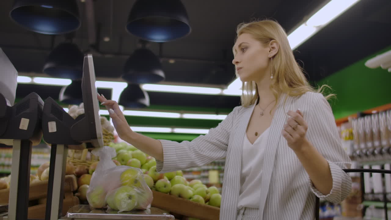 Young Woman Weighing Apples on the Electronic Scales. Housewife Shopping in a Supermarket in the Department of Fruit and Vegetables. Slow Motion. Sale Shopping Consumerism and People Concept
