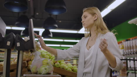 young woman weighing apples on the electronic scales. housewife shopping in a supermarket in the department of fruit and vegetables. slow motion. sale shopping consumerism and people concept