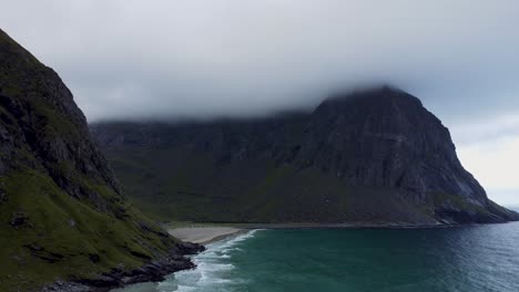 Flying-at-a-beach-in-Norway-overlooking-the-bay,-the-beach-and-the-mountains-that-are-partly-covered-in-clouds