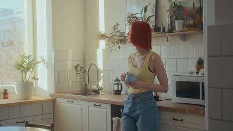 young girl drinking coffee and looking through window in sunlit kitchen