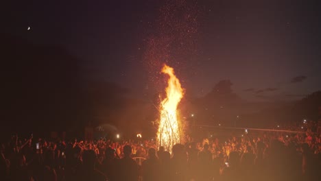 people stand around a big bonfire at a festival