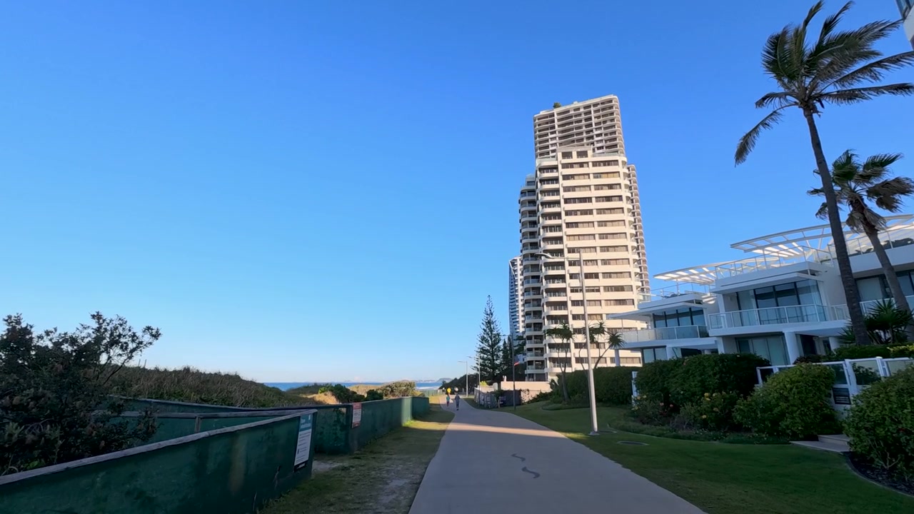 Ciclistas y peatones en un sendero costero cerca de edificios de apartamentos