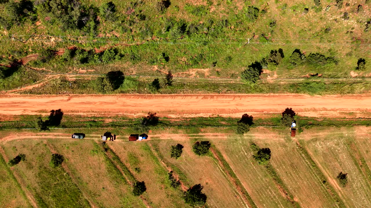 Top down drone view over tractors hauling crops from farm land next to dirt road