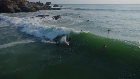 Vista-Aérea-Invirtiendo-A-Través-De-Surfistas-Montando-Olas-Poderosas-En-Punta-Zicatela-Océano-Pacífico-Iluminado-Por-El-Sol-Paisaje-Marino-De-Oaxaca