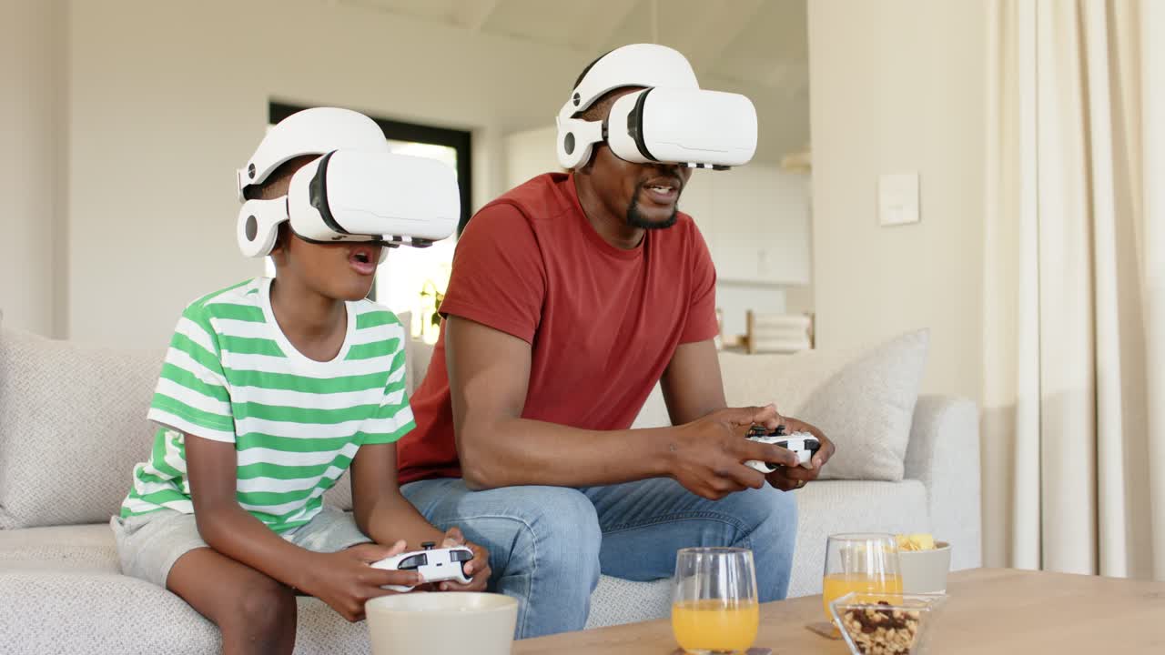 Padre e figlio afroamericani che prendono i controller, indossano le cuffie e giocano a un videogioco VR a casa
