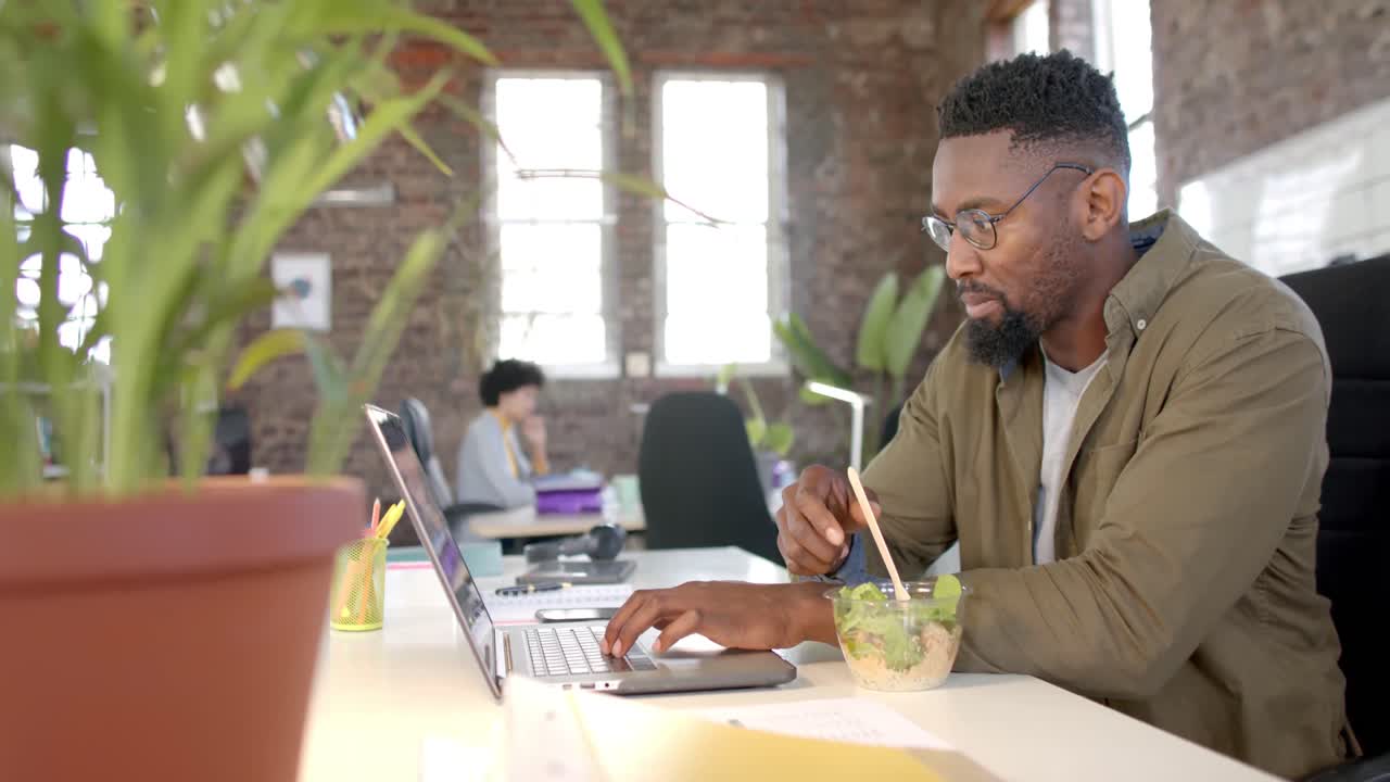 Focused diverse colleagues using laptop and having lunch in office in slow motion