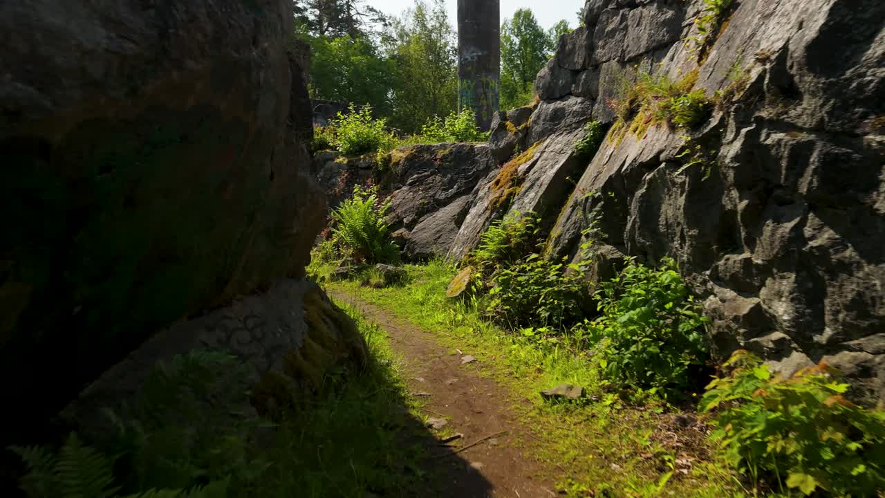 Low altitude aerial drone flight moving along narrow overgrown walkway towards historic Tureborg Castle ruins in Uddevalla Sweden on sunny day