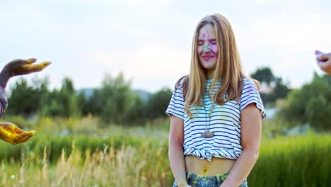 young pretty girl standing in the field and laughing while her friends tossing colorful paints in powder during holi fest