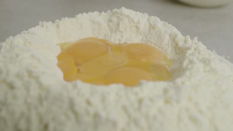 close up of egg yolks inside flour ring on kitchen cooking table