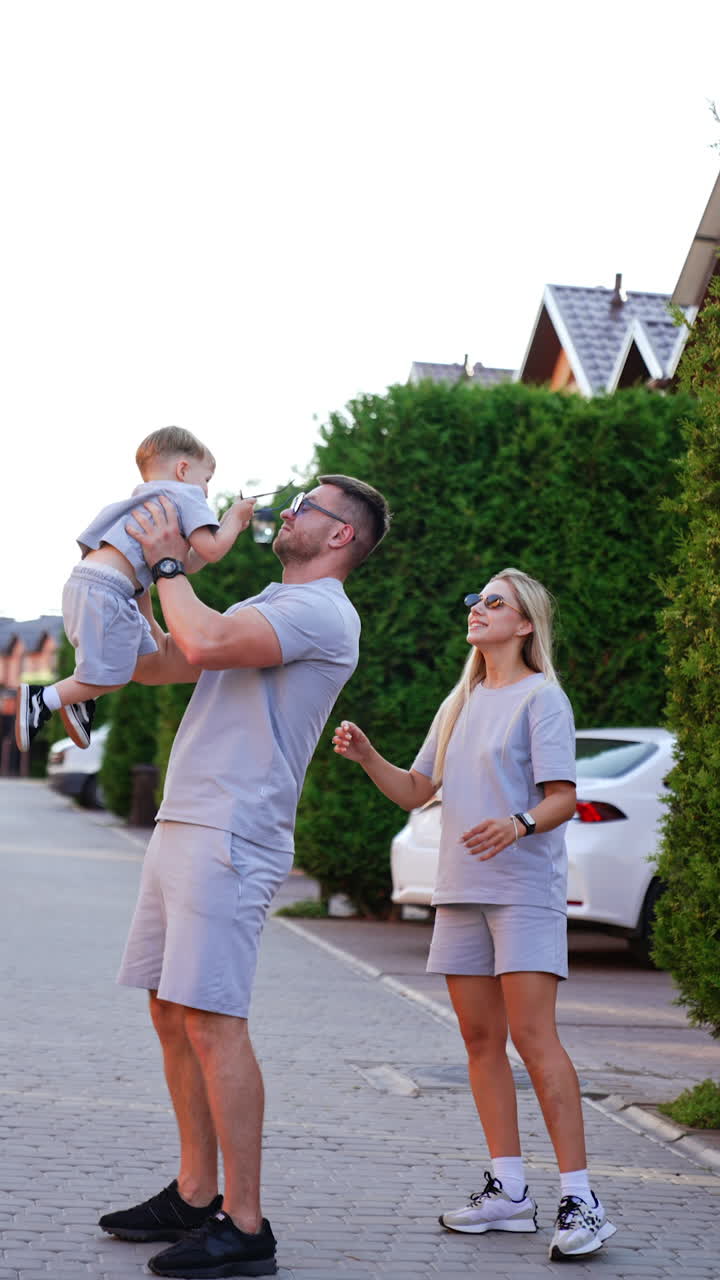 Kyiv, Ukraine, 25 May 2025: Family enjoying time together outdoors. Family members play with their child in a green residential area, near parked cars
