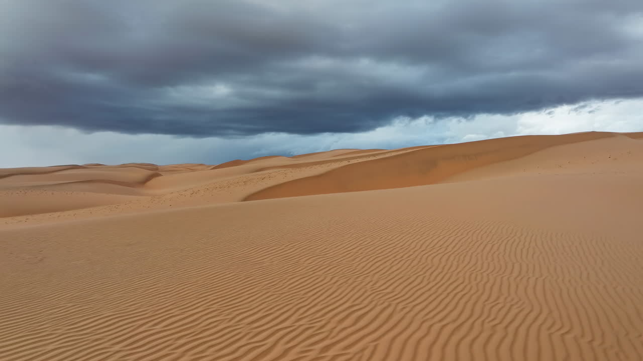 Nuvole temporalesche su dune di sabbia ondulate con cielo scuro e teso e motivi scolpiti dal vento, contrasto drammatico.