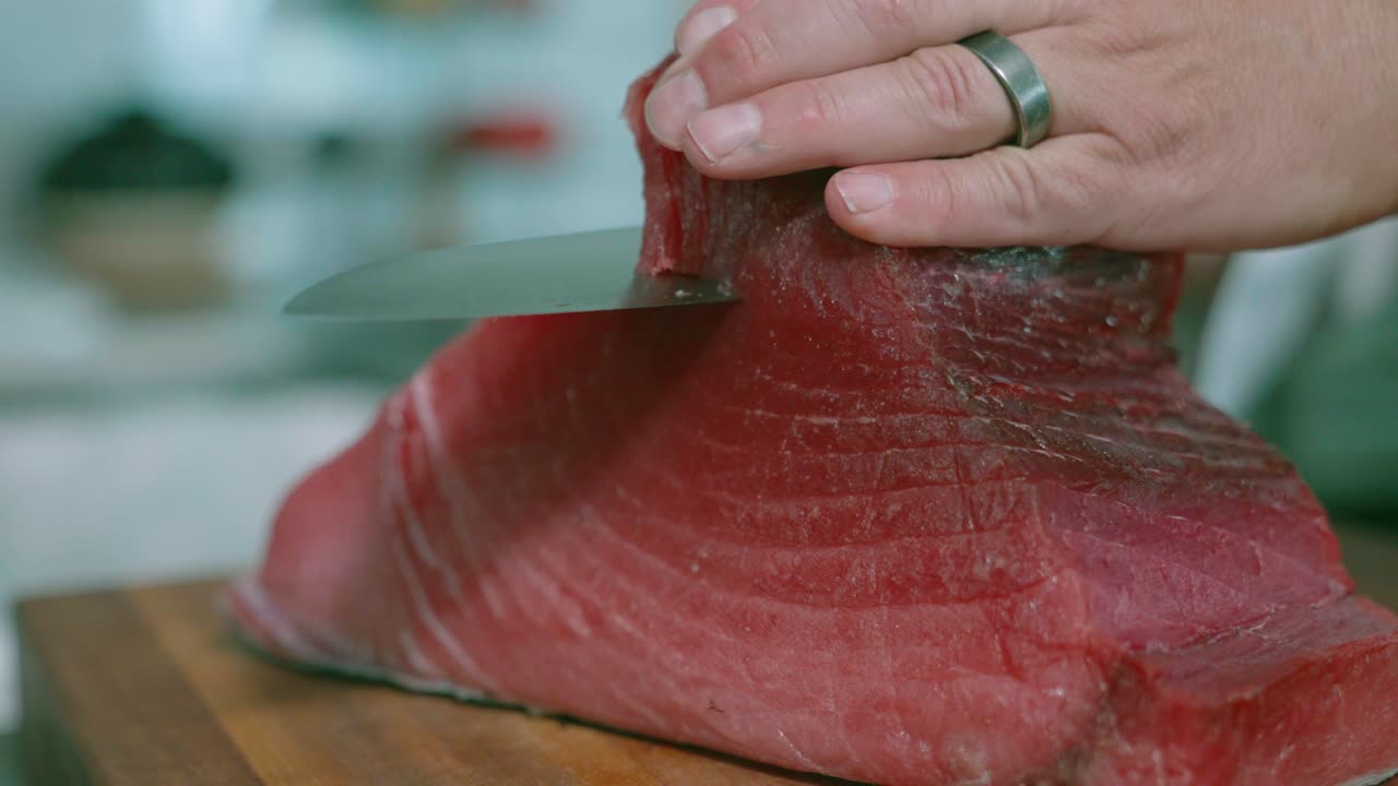 A static close-up shot captures a sushi chef trimming the top of a giant tuna slab, highlighting the precision and skill involved in sushi preparation. Ideal for culinary, sushi, and food preparation