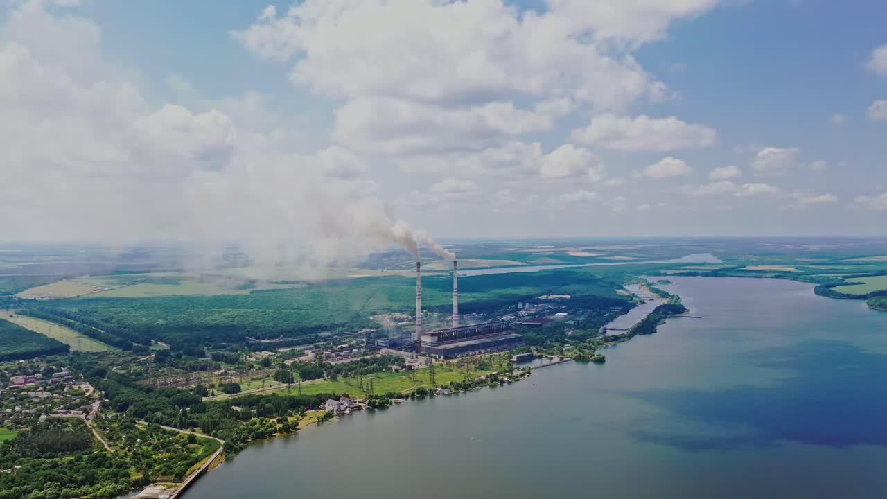 Natural environment of fields, forests, a wide river and factory polluting the air. Pipes with smoke from the big plant near the river. Ecological problem.