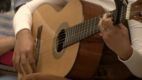 Primer-Plano-De-Una-Mujer-Hispana-Tocando-La-Guitarra-Acústica-En-Clase-De-Música