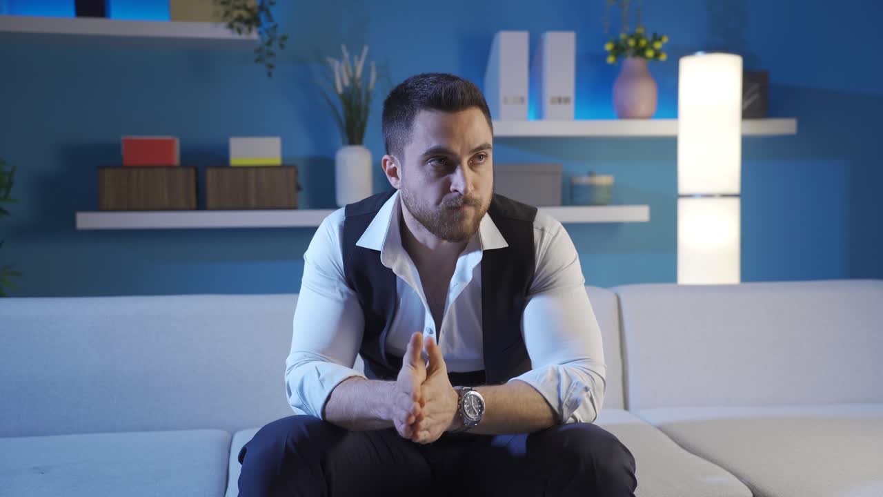 Stressed and worried young business man looking at watch in dark home room, nervous anticipation.