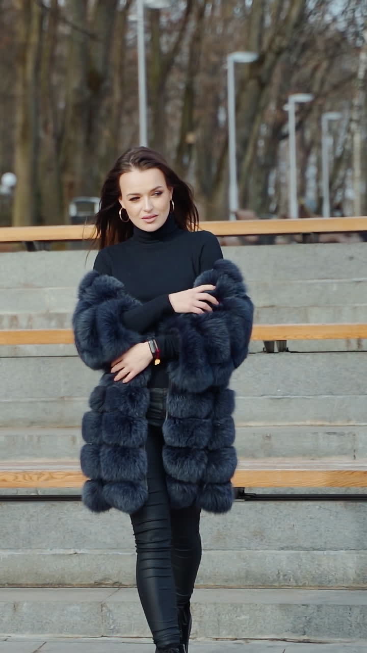 Beautiful model posing on camera in autumn park. Young woman in black fur coat walking and looking at camera. Slow motion. Vertical video