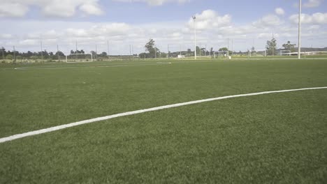 camera panning across lush green soccer field, revealing crisp white boundary lines and empty goal areas under bright summer sky with soft clouds