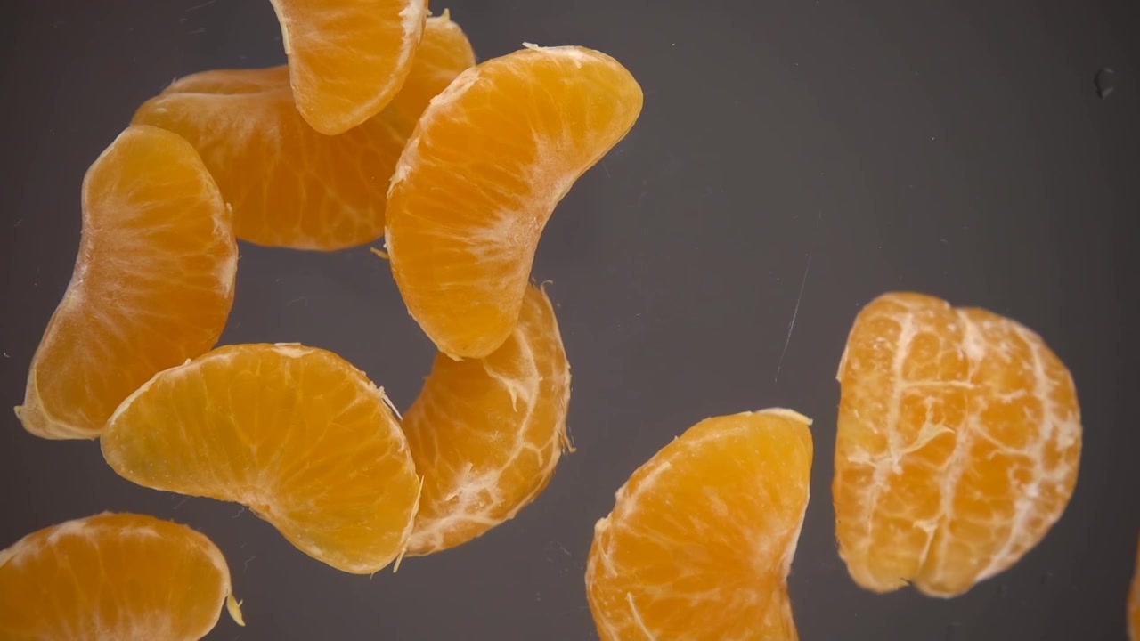 Fette di mandarini sbucciati cadono su una superficie di vetro. Vista dal basso. Slow motion
